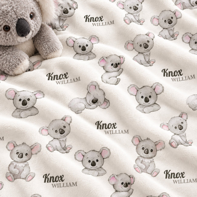 A close-up of a soft fleece blanket with an allover print of koala illustrations and the names 'Knox' and 'William' in black script. A plush koala toy is partially visible in the top left corner.