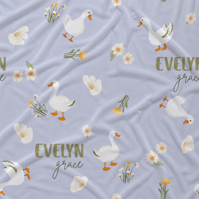 Light lavender fabric with a repeating pattern of white geese, small white flowers, green stems, and the words 'EVELYN grace' in muted olive green and dark script.