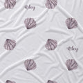 White fabric with a repeating pattern of watercolor-style lavender-gray seashells and the name 'Riley' printed in script.