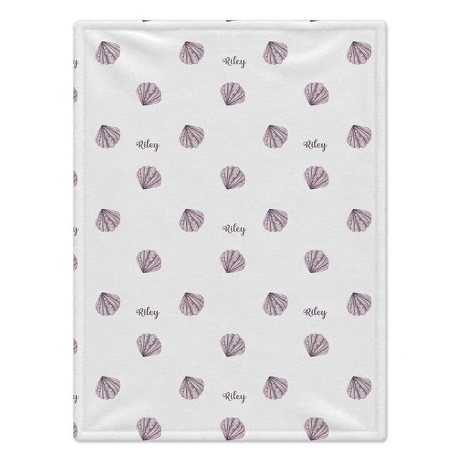 A personalized baby blanket with a white background, featuring a repeating pattern of purple seashells and the name 'Riley' printed in script.