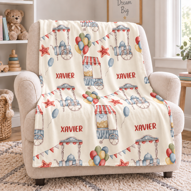 A personalized baby nursery accent chair draped with a cream-colored fleece blanket featuring a colorful carnival print and the name 'XAVIER' repeated in red.