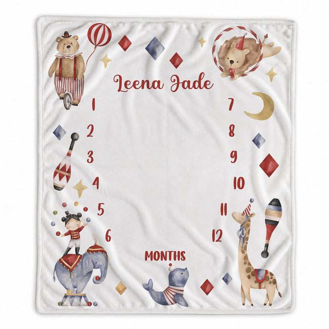 A personalized baby milestone blanket featuring circus-themed illustrations including a bear, elephant, giraffe, and sea lion, with a numbered months track from 1 to 12 and the custom name 'Leena Jade' in the center.