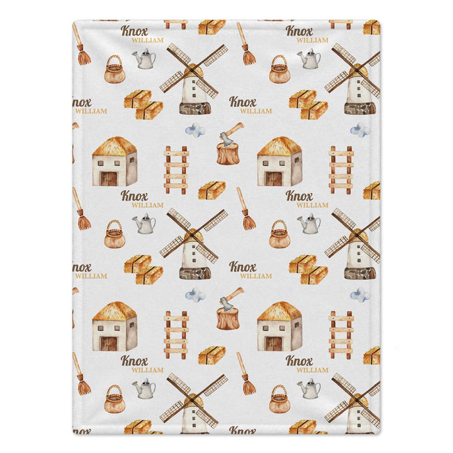 Personalized Farm Baby Blanket. Illustrated farm buildings, windmills, and countryside details surround a custom name in warm earthy colors.