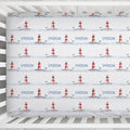 Personalized baby bedding set in a white crib, featuring a repeating pattern of red and white lighthouses, blue seagulls, and the name 'EMERSON' printed in blue.