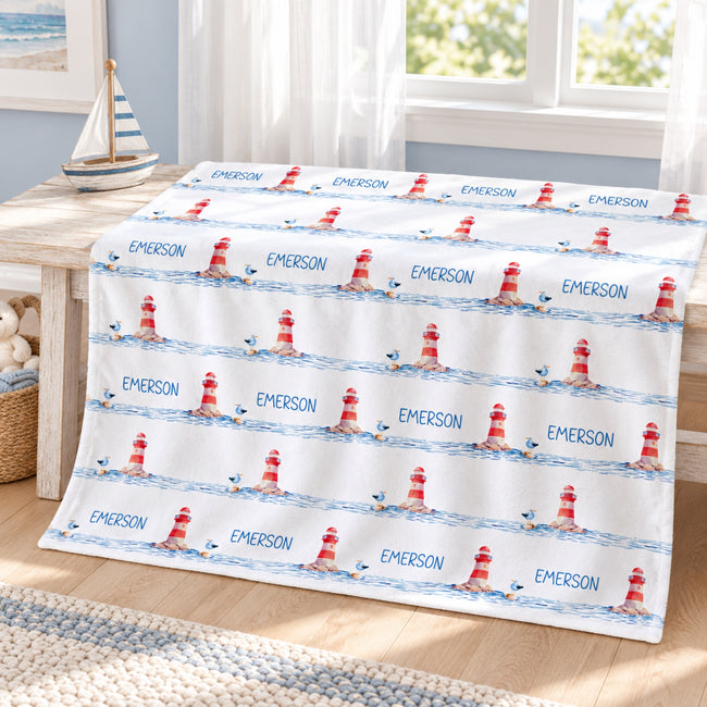 Personalized Lighthouse Baby Blanket. Red-and-white lighthouses, little seabirds, and blue watercolor waves create a coastal setting for a custom name.