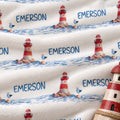 Personalized Lighthouse Baby Blanket. Red-and-white lighthouses, little seabirds, and blue watercolor waves create a coastal setting for a custom name.
