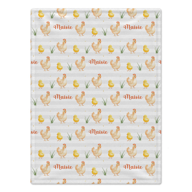 A rectangular fabric item, likely a baby blanket or towel, featuring a repeating pattern of watercolor-style chickens, yellow chicks, green grass, and the name 'Maisie' in orange script on a light gray and white striped background.