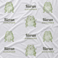 White fabric with a repeating pattern of green cartoon frogs and the custom text 'Kieran ALEXANDER' printed in dark green and gray.