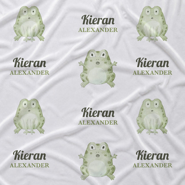 White fabric with a repeating pattern of green cartoon frogs and the custom text 'Kieran ALEXANDER' printed in dark green and gray.