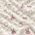 A close-up of a plush blanket with a personalized print featuring the name 'Avery Grace' in brown script, pink bows and dresses, and gold-toned rings on an off-white background.