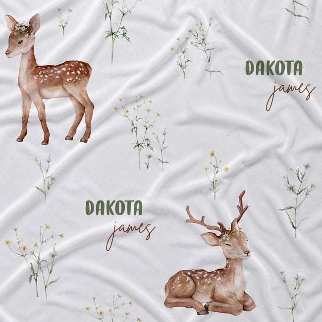 Personalized baby bedding fabric featuring watercolor deer illustrations and wildflower patterns on a white background, with the text 'DAKOTA james' printed in green and brown.