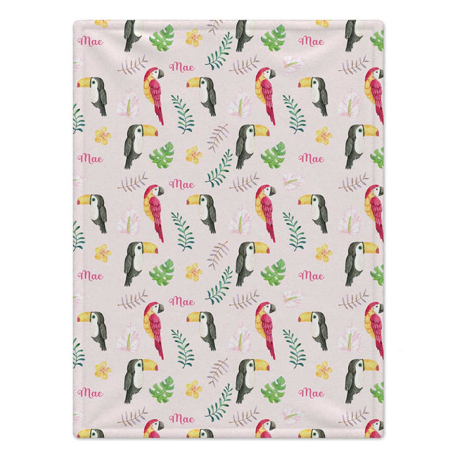 Personalized Tropical Bird Baby Girl Blanket. Colorful parrots, toucans, tropical leaves, and flowers surround a custom name on a soft pink background.