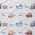 A white fabric surface printed with a repeating pattern of colorful children's vehicles and the name 'Oliver' in blue script. The vehicles include a train, boat, helicopter, car, and steam locomotive.