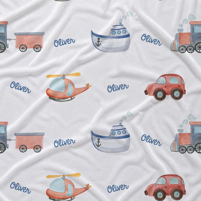 A white fabric surface printed with a repeating pattern of colorful children's vehicles and the name 'Oliver' in blue script. The vehicles include a train, boat, helicopter, car, and steam locomotive.