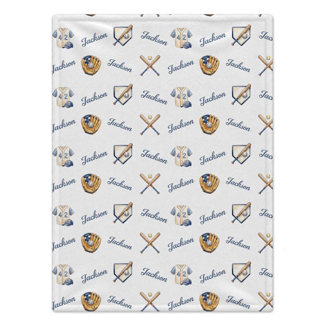 A white blanket featuring a repeating pattern of baseball-themed illustrations, including baseball uniforms, gloves, bats, and the name 'Jackson' in blue script.