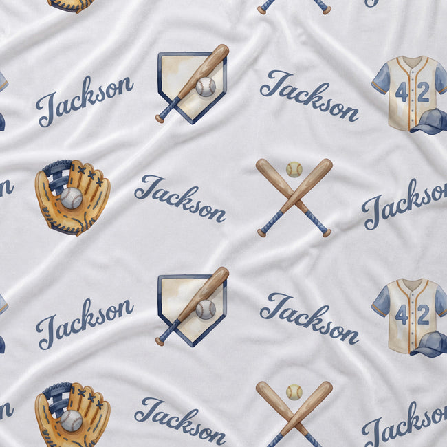 A close-up of a white fabric with a repeating custom baseball-themed pattern featuring the name 'Jackson' in navy script, crossed wooden bats, a baseball glove with a ball, a baseball bat in a helmet, and a baseball jersey with the number 42.