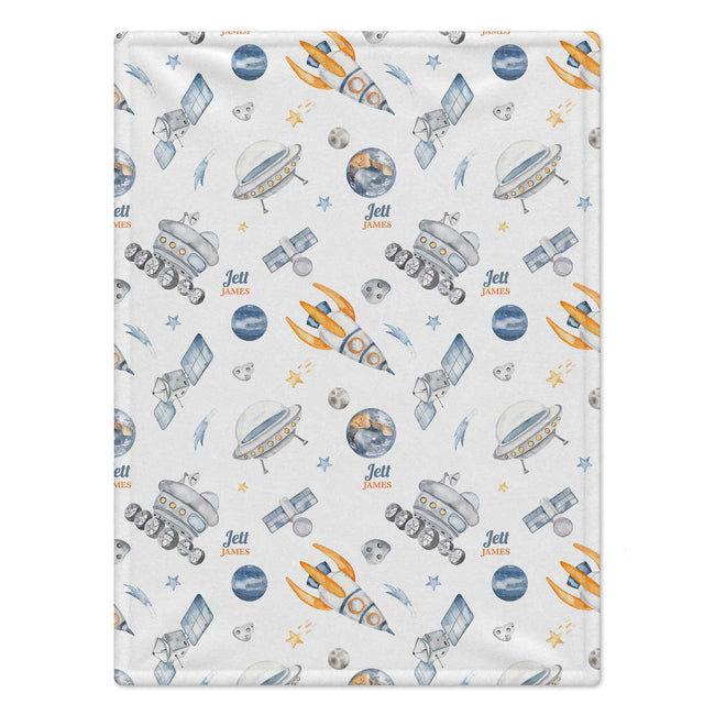 A personalized baby blanket featuring a space-themed pattern with planets, rockets, satellites, and stars. The design includes the custom text 'Jett James' repeated throughout on a light cream background.