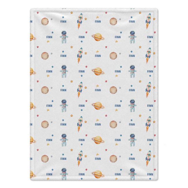 A square fabric item, likely a blanket or towel, featuring a repeating space-themed pattern with astronauts, rockets, planets, and stars on a light gray background.
