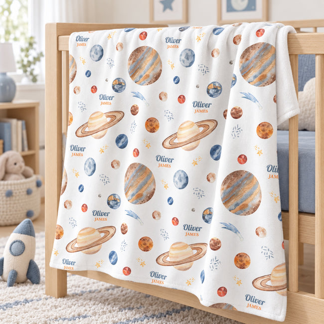 Personalized Planet Baby Blanket. Watercolor planets and celestial details surround a custom name in warm gold, blue, and earthy tones.