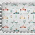 A personalized baby crib bumper sticker with a repeating pattern of cute cartoon animals in vintage cars, trees, and the names 'COLTON joseph'. The bumper sticker is shown fitted inside a white wooden crib.