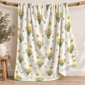 Ivory blanket with yellow daffodil clusters, scattered green leaves, and the name Clara Mae in gold and sage green lettering.