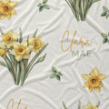 Ivory fabric with yellow daffodil clusters, scattered green leaves, and the name Clara Mae in gold and sage green lettering.