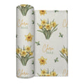 Ivory swaddle blanket with yellow daffodil clusters, green leaves, and the name Clara Mae in gold and sage green lettering.