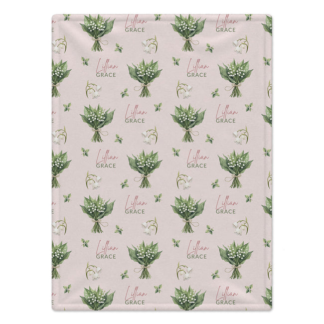 Pale blush blanket with white lily of the valley bouquets, green leaves, and the name Lillian Grace in rose and green lettering.