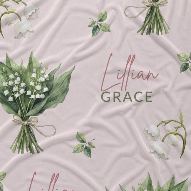 Pale blush fabric with white lily of the valley bouquets, green leaves, and the name Lillian Grace in rose and green lettering.