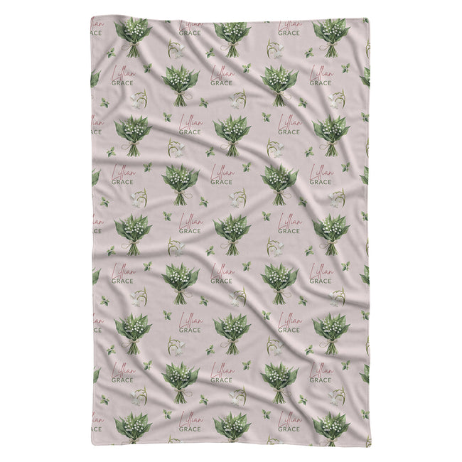 Pale blush swaddle blanket with white lily of the valley bouquets, green leaves, and the name Lillian Grace in rose and green.