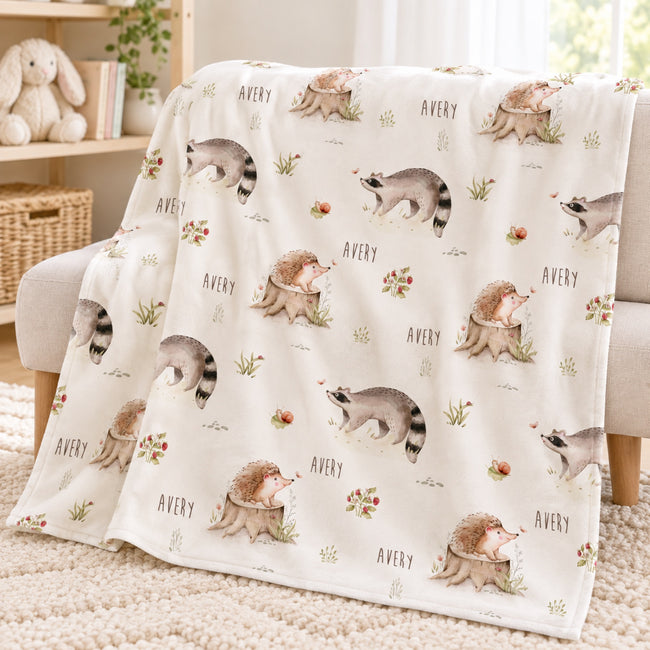 Personalized Woodland Animal Baby Blanket. Sweet hedgehogs, raccoons, snails, and meadow plants surround a custom name on a soft neutral background.