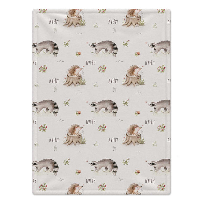 Personalized Woodland Animal Baby Blanket. Sweet hedgehogs, raccoons, snails, and meadow plants surround a custom name on a soft neutral background.