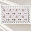 A fitted crib mattress with a repeating pattern of raccoons, squirrels, and the name 'AVERY' in a soft watercolor style, shown inside a white wooden crib on a light neutral floor.