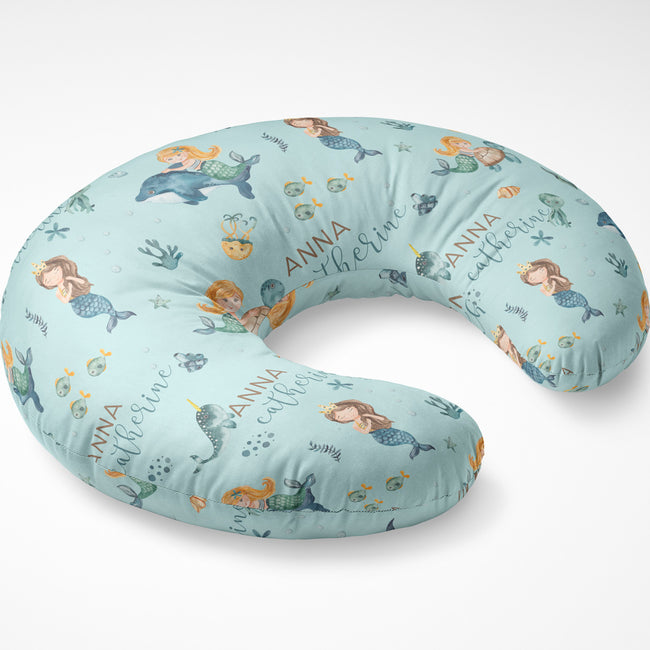 A U-shaped baby nursing pillow with a light blue mermaid and sea creature print, featuring the personalized name 'ANNA catherine' in script.