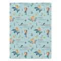 A personalized baby blanket featuring a light blue mermaid and dolphin pattern with the name 'Anna Catherine' printed in gold script.