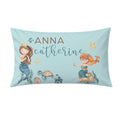 A personalized rectangular pillow featuring a light blue background with watercolor illustrations of two mermaids, a turtle, seashells, and the text 'ANNA catherine' in brown and teal lettering.