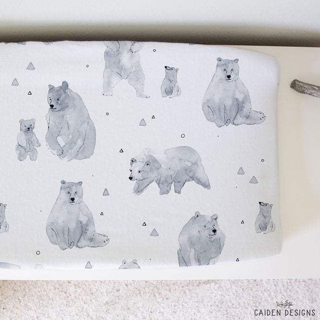 A baby changing pad cover featuring a watercolor-style print of polar bears and small geometric shapes on a white background, styled on a neutral surface.