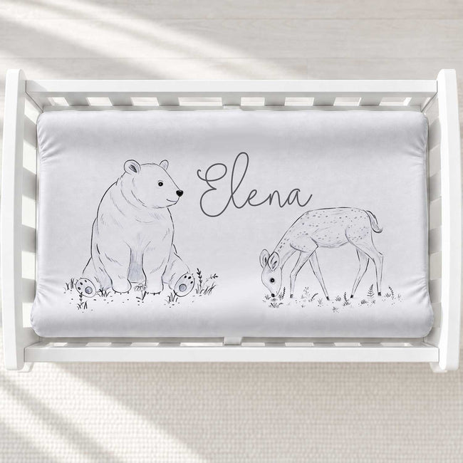 A personalized baby changing pad cover featuring a gray and white illustration of a polar bear, a deer, and the name 'Elena' in script.