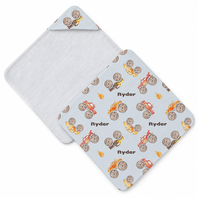 Pale blue hooded towel featuring colorful monster trucks with oversized tires, flame details, and the name Ryder in dark lettering.