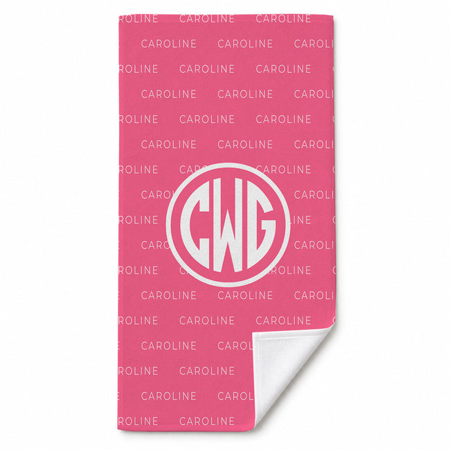 A pink beach towel with a repeating white 'CAROLINE' pattern and a large white circular monogram reading 'CWG'