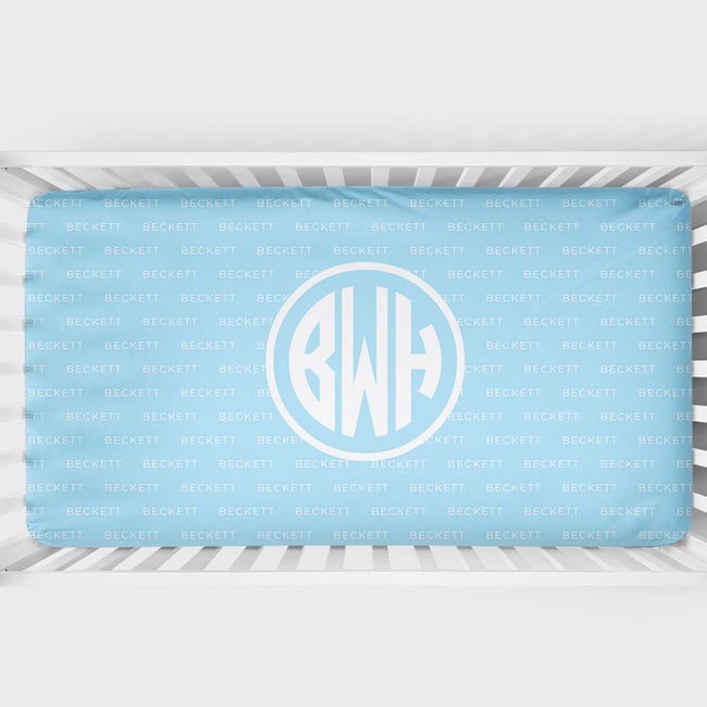 A light blue baby crib bedding set featuring a duvet cover and matching pillowcase with a repeating monogram pattern of 'BECKETT' and a large circular monogram 'BWH' in the center.