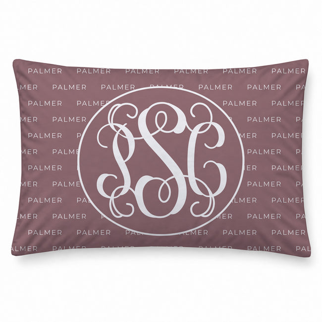 A pillowcase in dusty mauve with a white monogram design in the center, featuring a repeating 'PALMER' watermark pattern across the background.