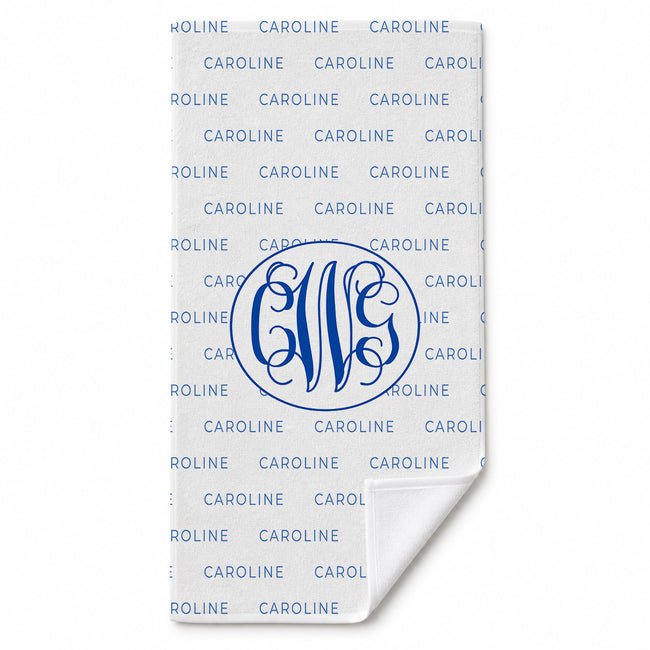 A white personalized towel featuring a repeating blue 'CAROLINE' pattern and a large blue monogram 'CWG' in the center, with the bottom corner folded over to show the white reverse side.