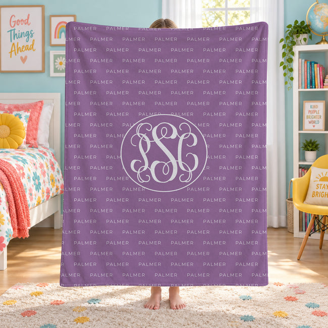 A person standing in a bedroom holding a purple blanket with a white monogram and repeated 'PALMER' text. The room includes a bed, yellow chair, bookshelf, and wall decor.