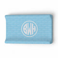 A light blue changing pad cover featuring a repeating 'BECKETT' pattern and a large central circular monogram with the initials 'BWH' in white.
