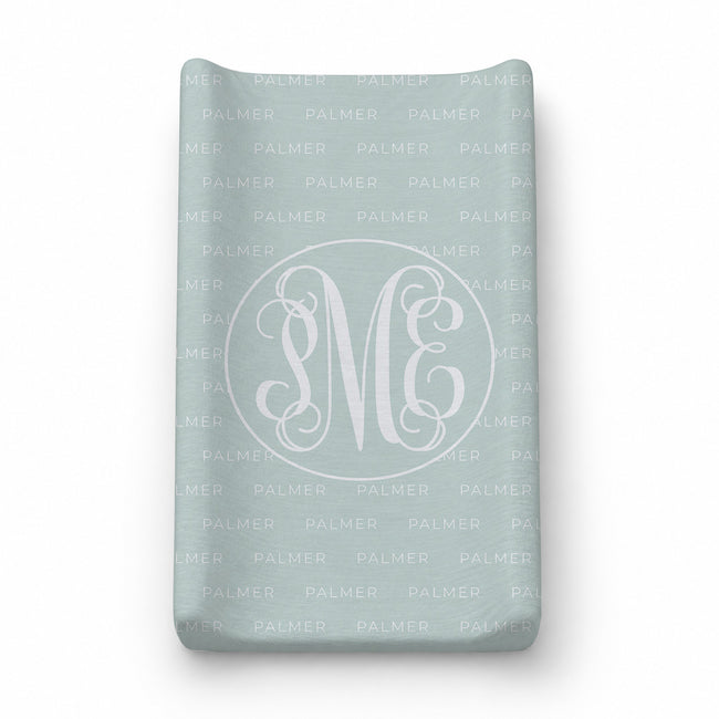 A personalized soft mint baby changing pad cover featuring a white monogrammed 'PME' design inside a circle with a repeating 'PALMER' personalization pattern.