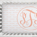 A close-up of a white crib sheet featuring a large peach-pink monogram letter 'S' inside a circle, with the brand name 'PALMER' repeated faintly in peach-pink text across the background.