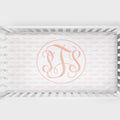 A crib sheet featuring a large peach monogram design in the center with the initials 'PS' in an elegant script. The background of the crib sheet is covered in a repeating light pink 'PALMER' brand watermark pattern.
