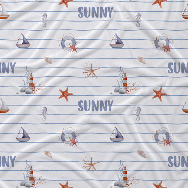 A close-up of a fabric surface with a nautical print featuring blue horizontal stripes, sailboats, seahorses, starfish, lighthouses, and the word 'SUNNY' repeated in blue.