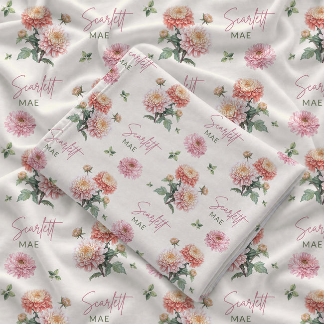 Ivory swaddle blanket with peach and pink chrysanthemums, green foliage, and the name Scarlett Mae in rose and green lettering.